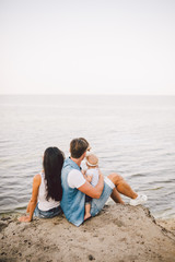 Theme family vacation with small child on the nature and sea. Mom, Dad and daughter of one year are sitting in embrace, girls in the hands of man, with his back at height of cliff overlooking the sea