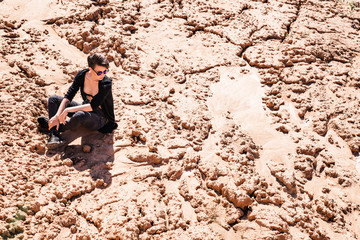 Fashionable girl sitting on the sand. Horizontal photo