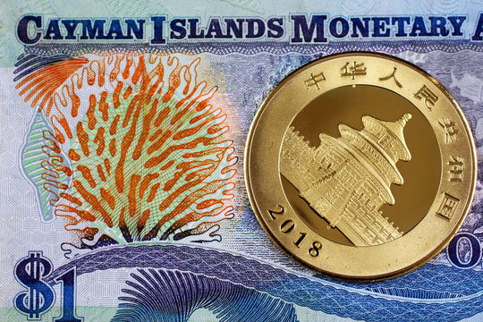 A close up image of a Chinese one ounce gold coin with a colorful Cayman Islands dollar bill