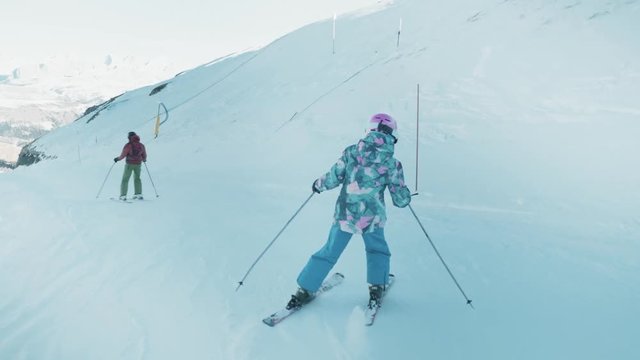 Gorgeous tacking shot of a young girl carving side to side down a ski slope on a sunny day.