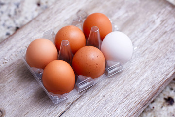 Six eggs plastic packing on wooden table. One different color of egg. Five brown and one white. 
