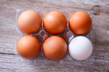 Six eggs plastic packing on wooden table. One different color of egg. Five brown and one white. 