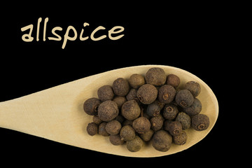 Allspice on wooden spoon isolated on black background