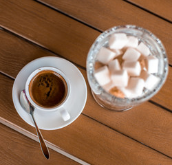 A small white porcelain espresso cup on a saucer with a teaspoon and two pieces of sugar