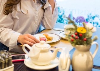 The hands of a woman who sits at a table with a cup of tea and macaroons in a cafe