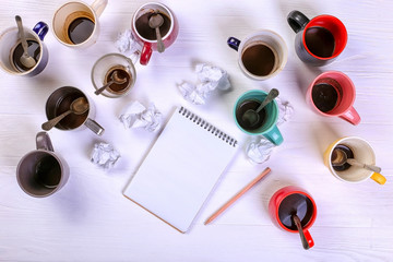 Empty dirty coffee cups, different colors on the table and a notebook for writing a letter. Concept caffeine dope, lack of energy to solve the problem. Copy space.