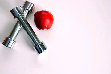 Two dumbbells and a red apple on a white table. Sports and proper nutrition.