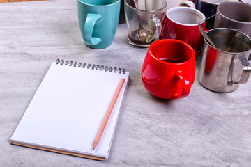 Empty dirty coffee cups, different colors on the table and a notebook for writing a letter. Concept caffeine dope, lack of energy to solve the problem. Copy space.