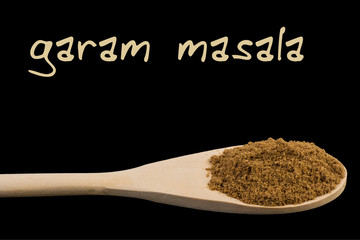 garam masala on wooden spoon isolated on black background