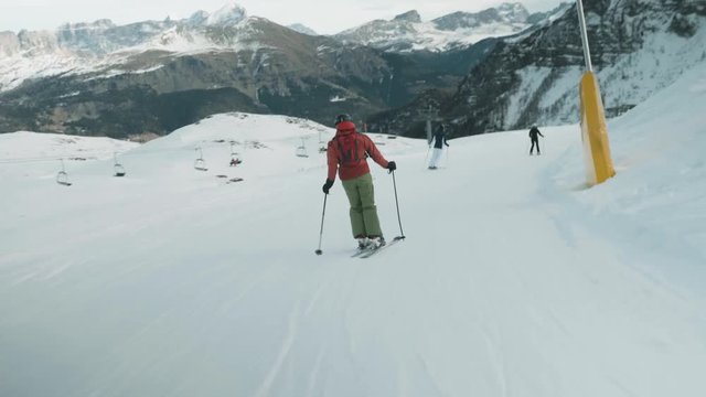 Following skiers downhill at Italian ski resort. Mountain range ahead in background.