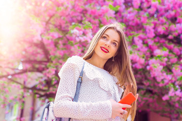 Close-up of a girl who holding a phone and over her pink flowers