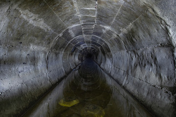 Flooded round underground drainage sewer tunnel reflecting in dirty sewage water