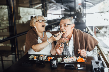 Content  couple seniors man and woman sitting at summer terrace eating sushi and spending time together happily