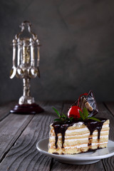 A biscuit cake is filled with chocolate with slices of chocolate tile, cherry and green leaf on wooden background.