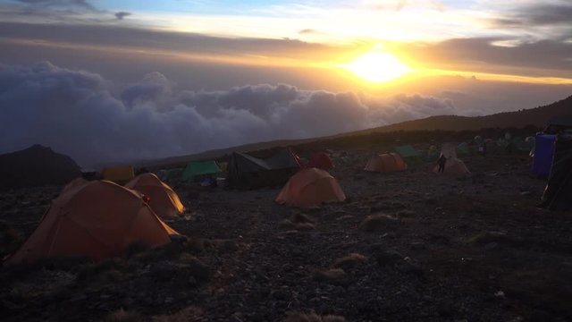 Beautiful Sunset at Mount Kilimanjaro Tent Camp with Thick Clouds. Multiple Tents and People. Shot from Great Height.