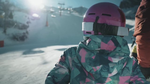 Over the shoulder shot of a young girl waiting at the bottom of a ski slope next to an adult family member. Dolomites, province of Belluno, Italy.