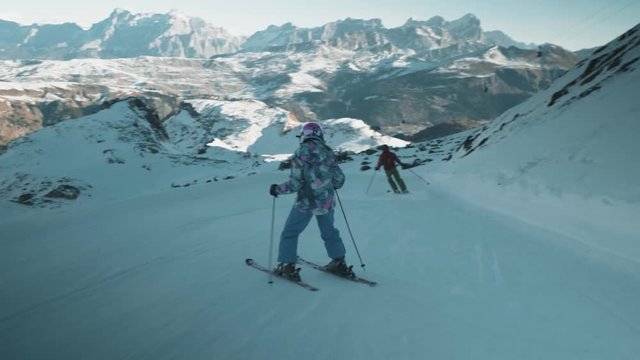Follow shot behind little girl travelling down ski slope. Mountain views in distance.