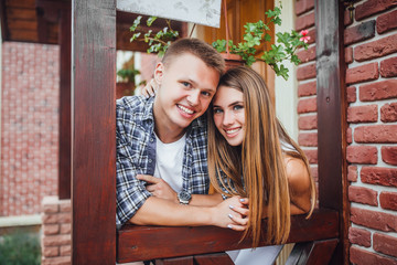 Young family standing at the porch of the house, hugging each other and looking at the camera. Happy smiling couple outside.