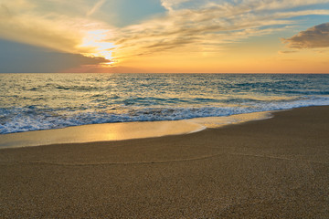 Fototapeta na wymiar Tropical sandy beach. Sunset seascape. Waves with foam hitting sand.
