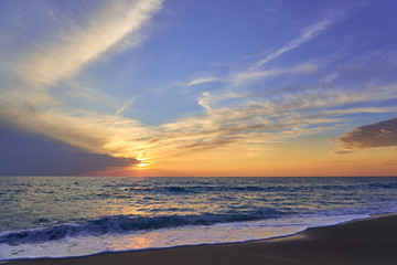 Naklejka na ściany i meble Tropical sandy beach. Sunset seascape. Waves with foam hitting sand.