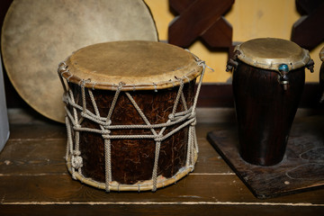 A large drum made of wood and leather,tied with twine. A small drum made of Buffalo leather and mahogany. National musical instruments, on the table, decorative wall background with wooden drawings.