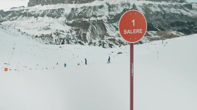 Route warning sign on ski route as skiers pass down slopes behind.
