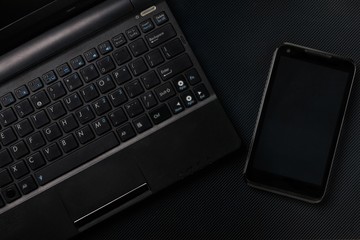 laptop with smartphone on black textured surface. flat lay