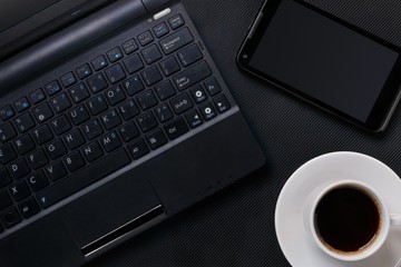 laptop with smartphone and cup of coffee on black textured surface. flat lay