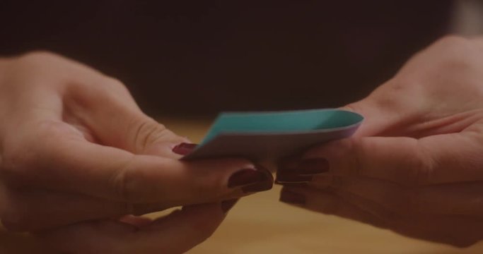 A woman's hands lift up a blue and purple note card and fold it in half.  The hands lift up a rusty single hole punch and punch a hole in the corner of the folded note card.