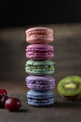 Beautiful and tasty French macaroon cookies stand on a wooden stand next to the fruit. Romantic dinner in the back of the house. Fast food menu background.