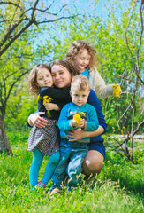 Naklejka na ściany i meble Mom with three children - boy and two girls smiling, and her children are hugging. Happy large family in nature.