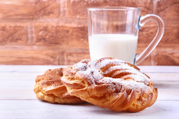 Chocolate and powdered sugar cream puff rings and glass with milk on wooden table. traditional Breakfast.