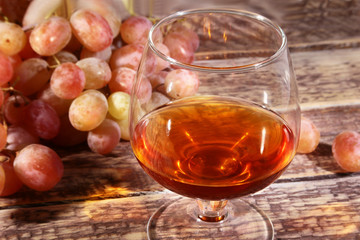 Glass with Cognac or Brandy and fresh grapes. still life in rustic style, vintage wooden background, selective focus.