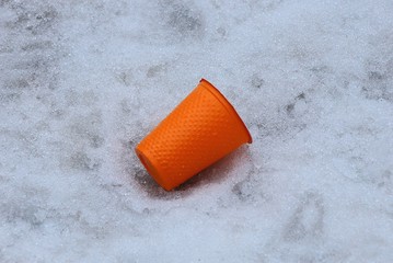 orange plastic cup litter lying on white snow outside