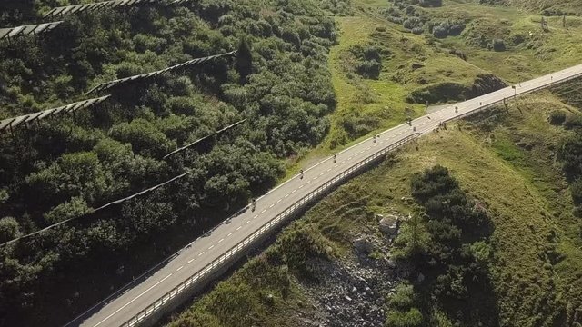 Aerial view of cyclists riding down the road in the Austrian Alps, in the Arlberg region, between Vorarlberg and Tyrol, on a sunny summer day.