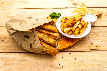 Fish and chips on wooden board in parchment paper on table. Traditional British food, close up, top view.