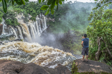View of man filming with an action camera, on a rock of the cascade of Kalandula, Angola