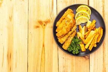 Fish and chips in black plate on wooden table. Traditional British food, top view