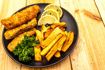 Fish and chips in black plate on wooden table. Traditional British food, close up