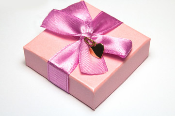 Golden heart pendant on pin paper box with a pink bow. Golden pendant in shape of heart without chain. St valentine's symbol and Valentine's Day Gift.