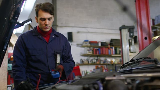 Car mechanic checking power voltage of car battery in the workshop