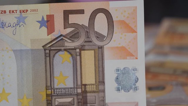 Macro close-up view slowly rotating around a 50 Euro bank note, currency with more in the background