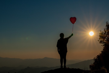 The silhouette of the girl and the balloon on the mountain at sunset