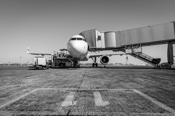 White wide body passenger aircraft with a boarding gate at the airport apron. Black and white....