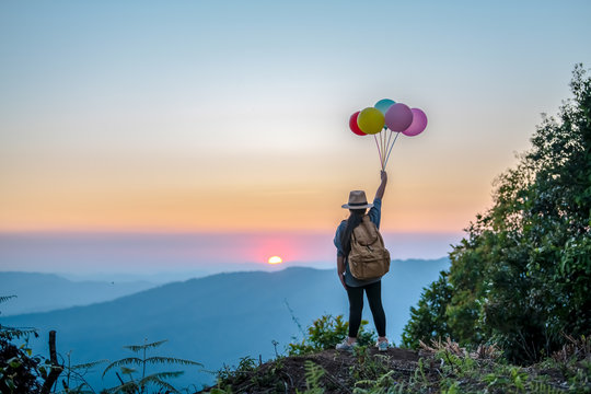 Asian girl with many colored balloons on the top of the mountain at sunset