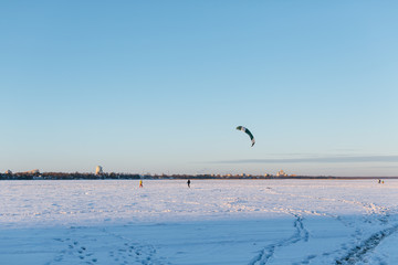 Outdoor photo of people involved in snow kiting/ winter kiting, kite skiing extreme sports, snow field with kite, frozen lake, frosty winter day, blue sky without clouds/ winter season concept.