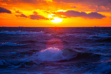 Fototapeta na wymiar rich bright orange sun in a cloudy sky over the sea during sunset