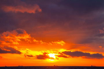 rich bright orange sun in a cloudy sky over the sea during sunset