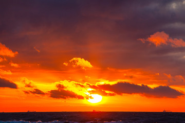 rich bright orange sun in a cloudy sky over the sea during sunset
