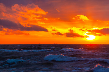 Obraz premium rich bright orange sun in a cloudy sky over the sea during sunset